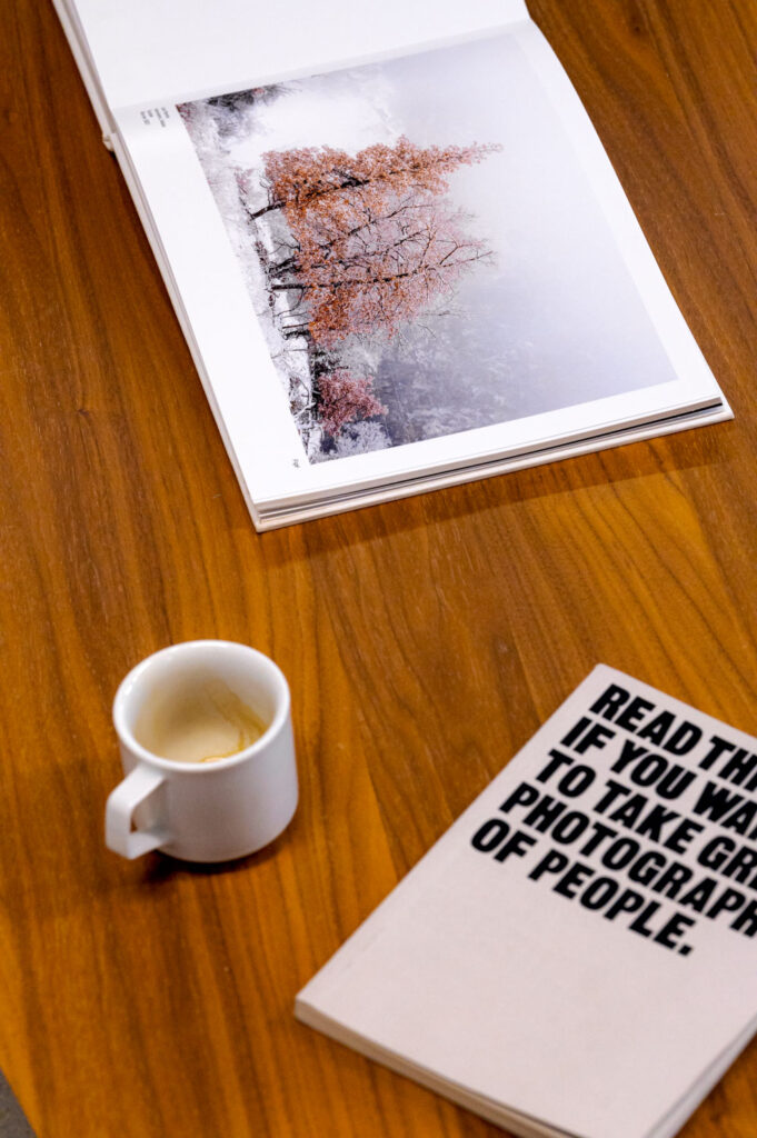 un livre photo ouvert et un deuxième fermé avec une tasse à café consommé au milieu, le tout sur une belle table en bois.